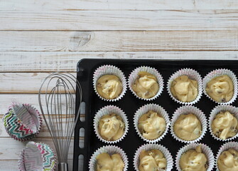 Paper tins with spread out dough for small muffins on baking trays from the kitchen oven, prepared for baking. Food background.