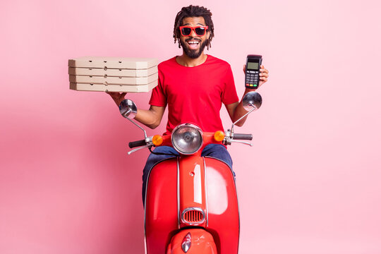 Portrait Of Handsome Cheery Guy Riding Moped Delivering Pizza Holding In Hand Terminal Wireless Pay Isolated Over Pink Color Background