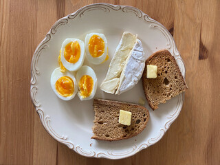 Breakfast Plate with Brie Cheese, Boiled Eggs and Butter Bread on Wooden Table.