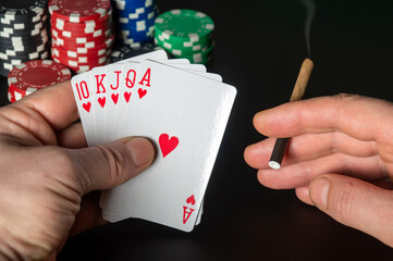 Poker cards royal flush combination. Close up of a gambler hand is holding playing cards and sigar in poker club