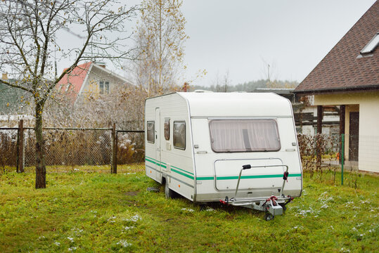 White caravan trailer on a green lawn in a village (camping site). Autumn landscape. Europe. Lifestyle, travel, tourism, road trip, journey, vacations, recreation, transportation, RV, motorhome