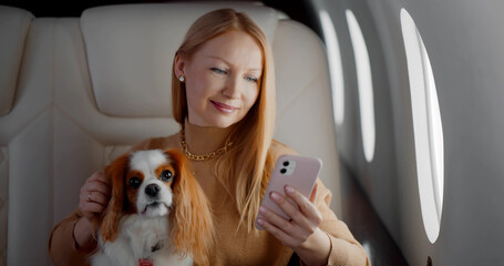 Beautiful rich woman with dog using smartphone in private first class plane