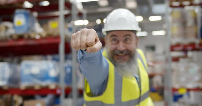Portrait of funny senior industrial worker in uniform posing as superhero in warehouse