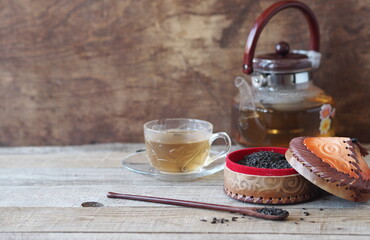 Composition of Asian medicinal herbal tea. A box with natural leaves of a tea plant, a medicinal herb and a teapot with a tea cup of brewed drink.