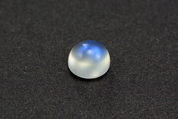 Natural adularia blue sheen round cabochon moonstone. Loose gem on gray textured leather background. Feldspar mineral group. Semiprecious gemstone not common relatively rare and expensive specimen