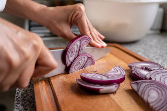 Chef cutting red onion into half thick slices with his kitchen knife.