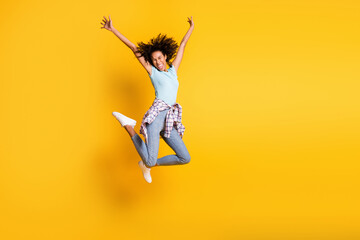 Full length photo of shiny funky dark skin curly girl dressed blue t-shirt jumping empty space isolated yellow color background