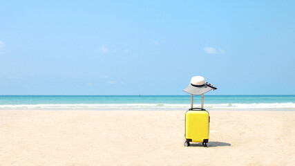 Travel on Summer and tourist planning with yellow suitcase with white hat fashion in the beautiful beach. Travel in holiday. Blue sky and sand background, on travel in summer concept.