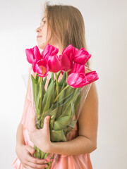 Portrait of a beautiful young girl in dress holding big bouquet of tulips isolated over white background