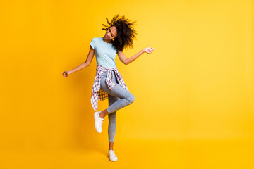 Full length photo of cute carefree dark skin curly girl dressed blue t-shirt dancing empty space isolated yellow color background