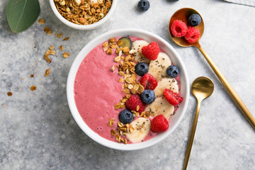 Summer acai smoothie bowls with raspberries, banana, blueberries, and granola on gray concrete background. Breakfast bowl with fruit and cereal, close-up, top view, space for text