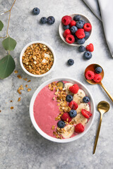Summer acai smoothie bowls with raspberries, banana, blueberries, and granola on gray concrete background. Breakfast bowl with fruit and cereal, close-up, top view, space for text