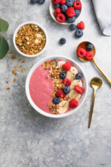 Summer acai smoothie bowls with raspberries, banana, blueberries, and granola on gray concrete background. Breakfast bowl with fruit and cereal, close-up, top view, space for text