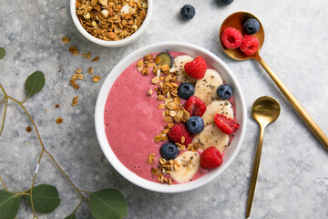 Summer acai smoothie bowls with raspberries, banana, blueberries, and granola on gray concrete background. Breakfast bowl with fruit and cereal, close-up, top view, space for text