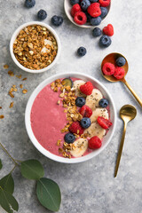 Summer acai smoothie bowls with raspberries, banana, blueberries, and granola on gray concrete background. Breakfast bowl with fruit and cereal, close-up, top view, space for text
