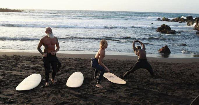 Multi generational surfer people doing warm up at the beach  before surf session- Multiracial men, lifestyle and sport concept