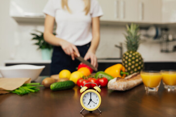 Obraz na płótnie Canvas Cropped shot of woman cooking vegetables salad for dinner. FOCUS on little yellow clock on the table.