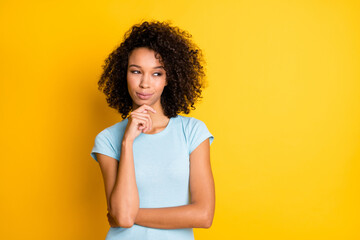 Fototapeta na wymiar Photo of cute thoughtful dark skin girl dressed blue t-shirt looking empty space arm chin isolated yellow color background