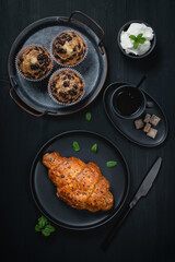 Cup of coffee, muffin and croissant on wooden black table
