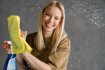Happy blonde woman maid holding bottle of detergent