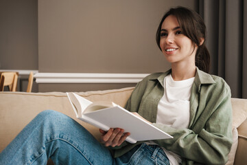 Obraz premium Portrait of a happy young woman sitting on couch with book