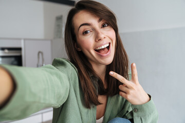 Young happy woman showing peace sign while taking selfie photo