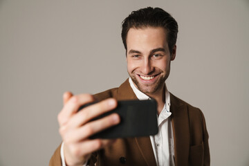 Unshaven brunette man smiling and taking selfie on cellphone