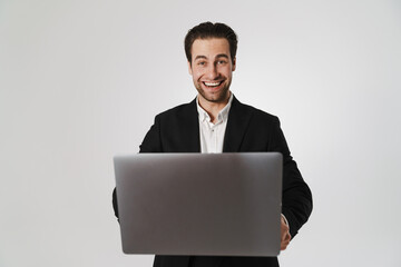 Unshaven brunette man in jacket smiling while using laptop