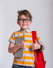 Portrait of happy school boy with backpack isolated against white background. Smiling face in glasses. Blond child in striped shirt with tablet in hands. Back to school