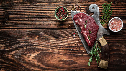 Raw rump steak on old meat cleaver on dark wooden background. banner, menu recipe place for text, top view