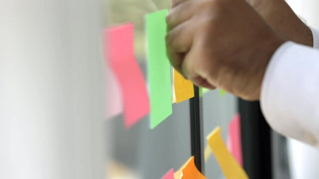 Business male hand put the Colorful of post it on the wall. sticky note or paper note on the windows for note what to do in the office.