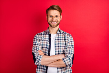 Fototapeta premium Photo of pretty confident young gentleman dressed plaid shirt spectacles hands folded smiling isolated red color background