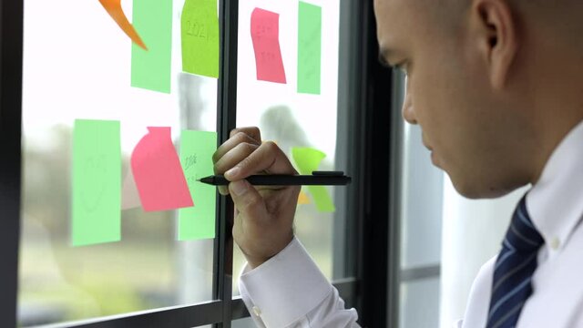 Business male writing note on the Colorful of post it on the wall. sticky note or paper note on the windows for note what to do in the office.