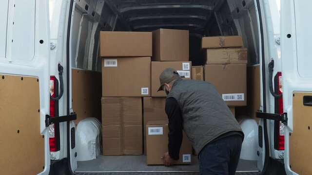 Young man shipper with his van during the delivery round in the global pandemic from Covid-19 Coronavirus wearing face mask while checking address with smartphone