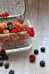 colorful forest fruits, small apricots and flowers, arranged raspberries, red currants and blueberries, natural vitamins, glass box filled with fruit, old, retro box made of hewn glass

