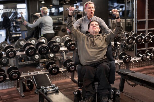 Man on wheelchair training in gym with personal trainer