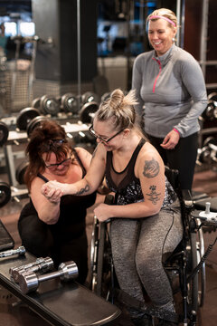 Woman on wheelchair training in gym with personal trainer