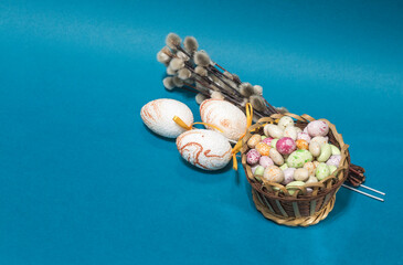 decorative Easter eggs with round candies in a basket and willow branches, on a blue background