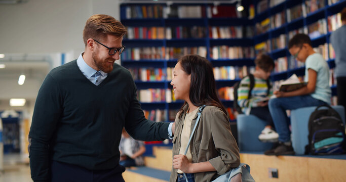 Male Teacher And Asian Schoolgirl Sharing High Five Standing In Library