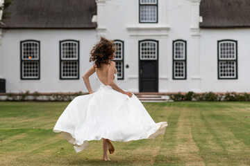 Barefoot bride running on a lawn in front of historic house