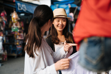 two girl friends together spend time travel together in summer bangkok thailand. Two beautiful woman make purchases in outdoor clothing store vendor in market. female point showing sister shopping