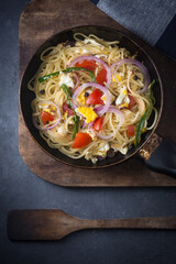 cooked spaghetti dish with egg, tomatoes, onions and green chilies on a pan, spaghetti pasta dish on a dark background