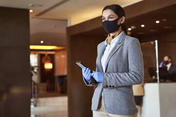 Fototapeta na wymiar Receptionist with modern gadget wearing rubber gloves and mask