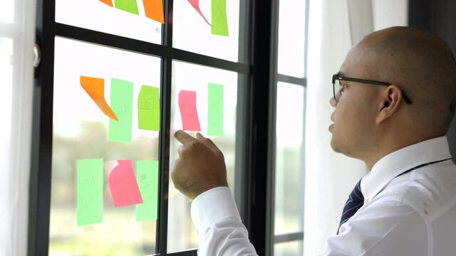 Business male hand pick the Colorful of post it at the wall. sticky note or paper note on the windows for note what to do in the office.