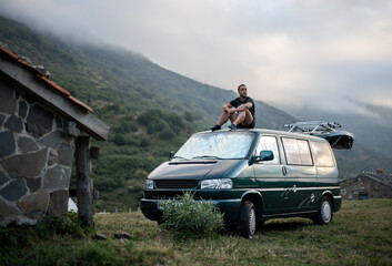 Young man sitting on the roof of his green camper van © Miguel Serrano