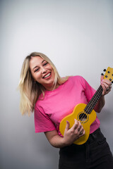 Fototapeta premium Young cheerful Caucasian female from Spain playing ukulele against a white wall