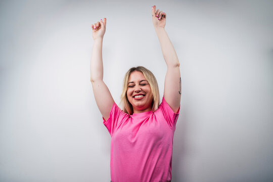 Young happy Caucasian female from Spain in a pink shirt showing peace gesture against a white wall