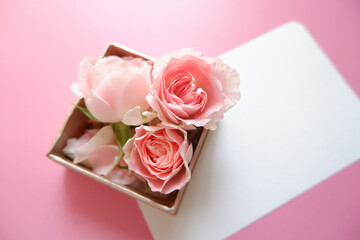 Spring greeting concept. Pink roses gift box with blank greeting card on pink background. Wedding,...