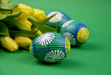 Fototapeta na wymiar Beautiful hand painted easter eggs with yellow tulips stock images. Easter colored eggs isolated on a green background with copy space for text stock photo. Traditional easter unique eggs