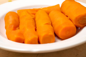 Six whole boiled carrots are in a white bowl, macro